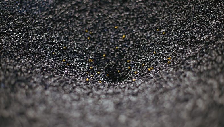 Nahaufnahme von schwarzen Kunststoffgranulaten mit vereinzelten gelben Körnern